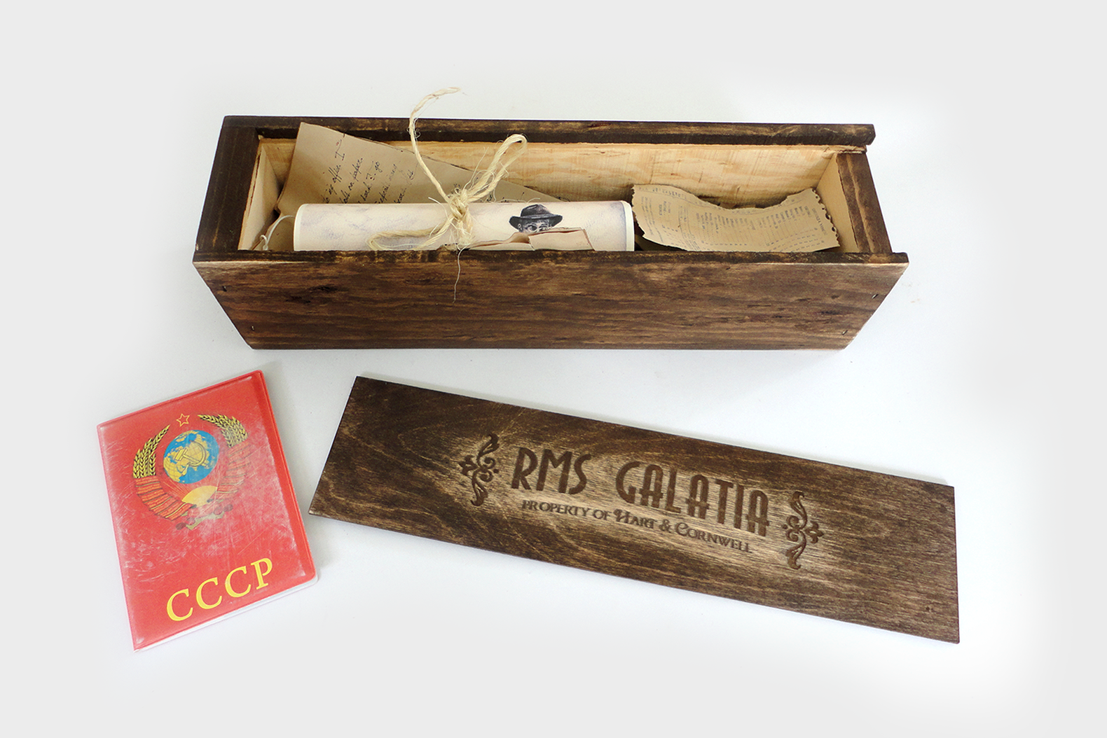 An image of a box that says RMS Galatia. Inside the box is a painting and various scraps of old paper documents, alongside a passport from the Soviet Union from the Blackhollow Project experience.